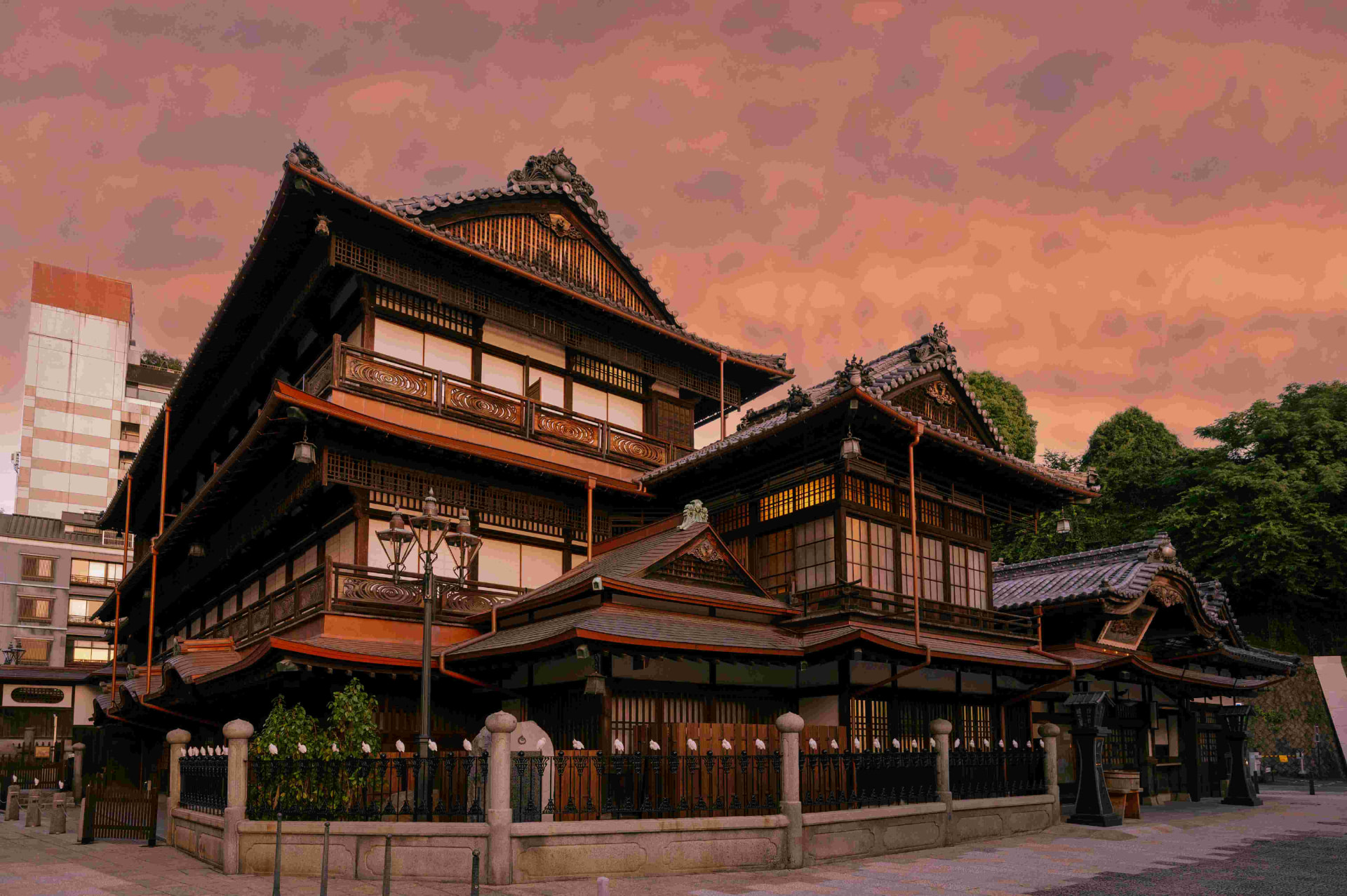 Dogo Onsen Honkan at dusk, lanterns lit, figures in yukata